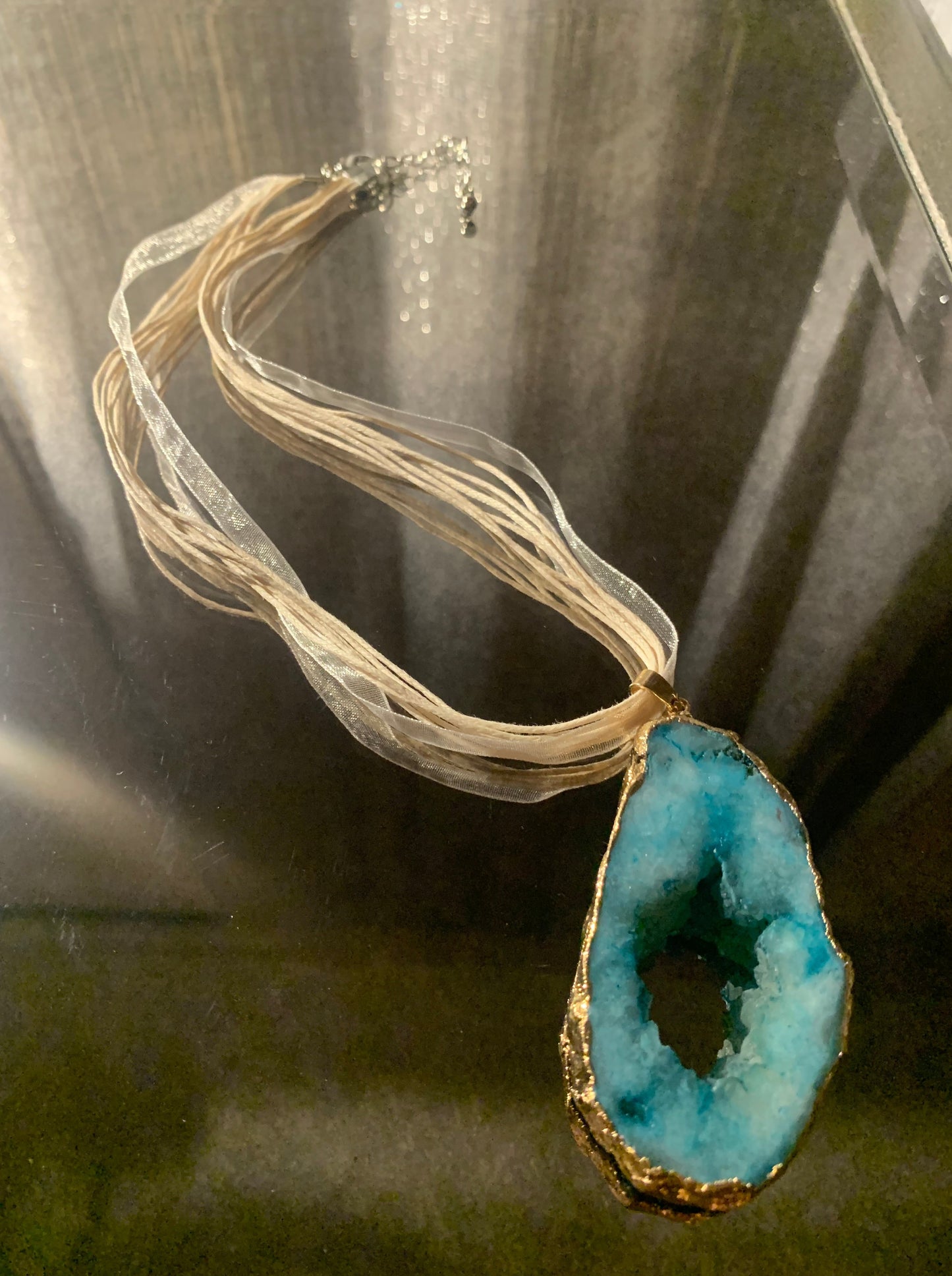 Necklace, Natural Turquoise Cratered Stone Pendant Trimmed in Gold Accented with Ivory and Cream Nylon Ribbon and Cords 18" Necklace with lobster clasp and extension chain.