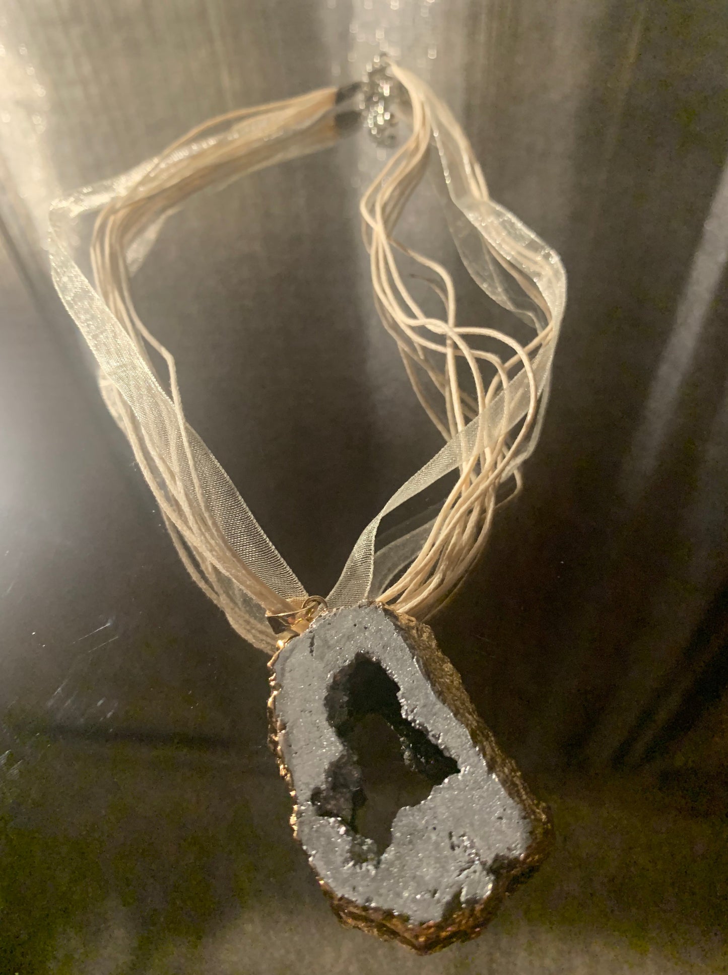 Necklace, Natural Pewter Cratered Stone framed in gold accented with 18" shimmer nylon ribbon multi cord finished with lobster clasp and extension chain.